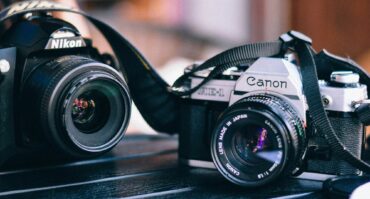 A nikon and canon camera on a black table
