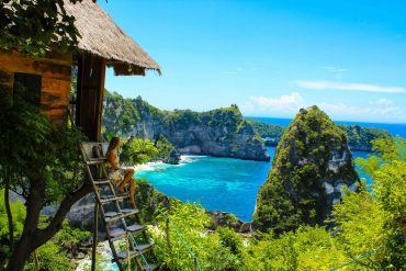 A female sitting on the steps of a hut overlooking the ocean