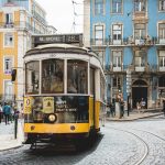 A tram in Lisbon, Portugal with blue and yellow buildings in the distance.