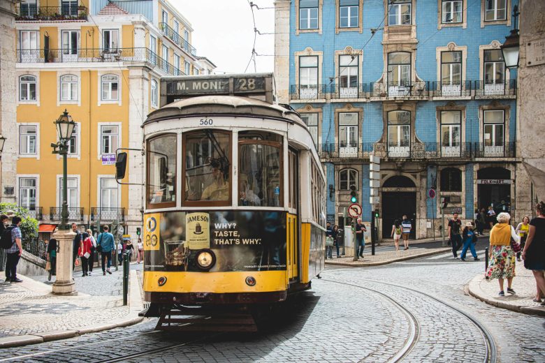 A tram in Lisbon, Portugal with blue and yellow buildings in the distance.